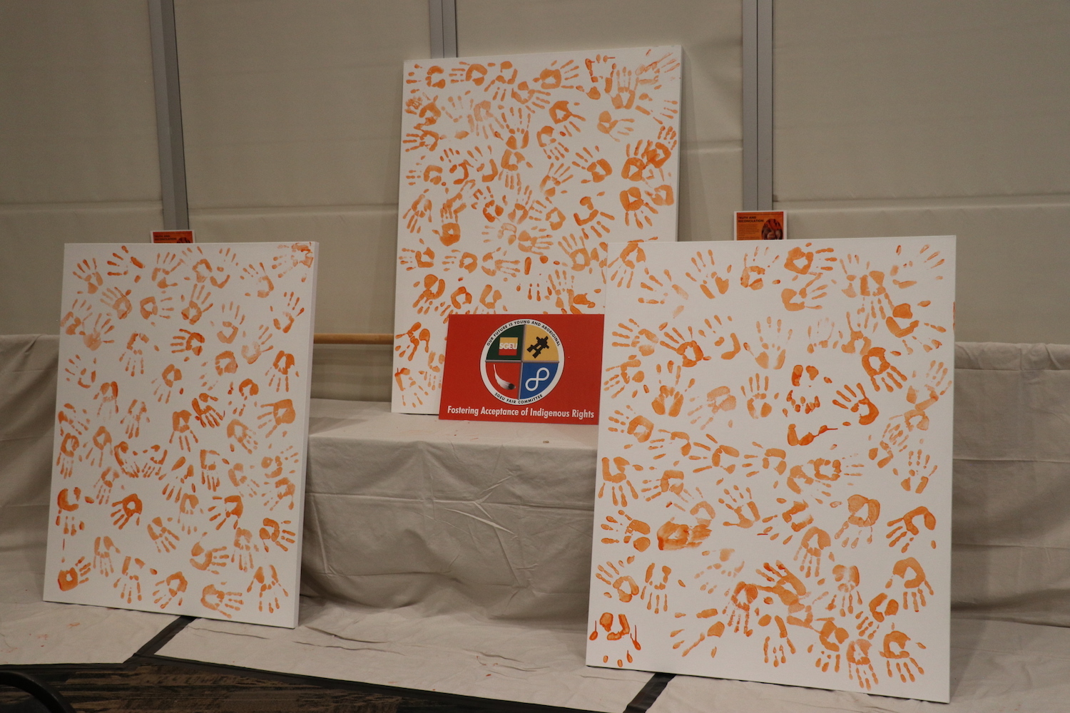 Three canvases filled with orange hand prints.